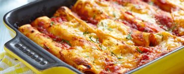 Yellow baking dish filled with tomato and cheese topped cannelloni